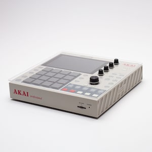 May include: A white Akai professional drum machine with a clear plastic cover. The drum machine has a black screen, 16 red pads, and several knobs and buttons.
