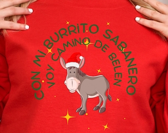 May include: A bright red crewneck sweatshirt featuring a central graphic of a grey donkey wearing a red and white Santa hat. The text "CON MI BURRITO SABANERO VOY CAMINO DE BELEN" is printed in green in a circular arc around the donkey, accented by yellow stars.