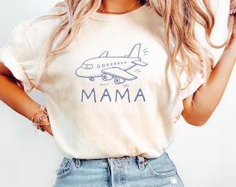 May include: An ivory short-sleeve t-shirt featuring a blue line-art illustration of a small airplane centered on the chest. Below the airplane graphic, the word MAMA is printed in a matching blue, sans-serif, uppercase font style.