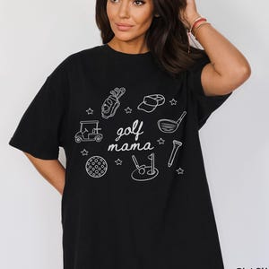 Puede incluir: Camiseta negra con un dise&ntilde;o gr&aacute;fico blanco de equipo de golf y el texto "golf mama".