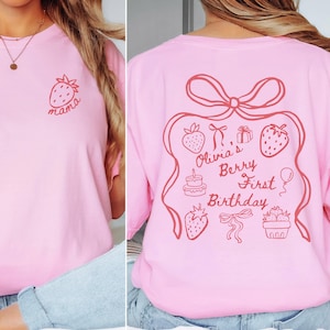 May include: Pink t-shirt with a strawberry and the word "mama" in red on the front. The back features a red outline of a gift with strawberries, a cake, and the text "Olivia's Berry First Birthday".