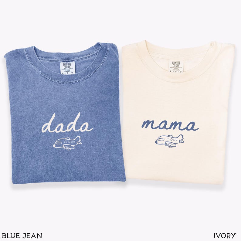 以下が含まれることがあります： 半袖Tシャツ2枚。ジーンズブルーのシャツには白い文字で「dada」と白い飛行機のグラフィックが、アイボリーのシャツには青い文字で「mama」と青い飛行機のグラフィックがプリントされています。どちらもComfort Colorsのラベルが付いています。