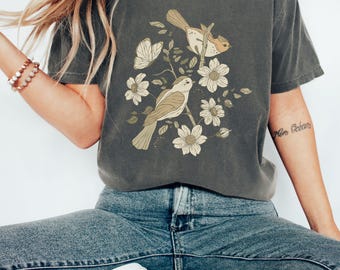 May include: A charcoal grey t-shirt with a vintage-style illustration of two birds perched on a branch with flowers. The birds are brown and beige with a light brown background.