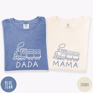 May include: Two Comfort Colors t-shirts, one blue jean and one ivory, each with a train graphic. The blue shirt says "DADA" and the ivory shirt says "MAMA". Both shirts have the Comfort Colors logo.