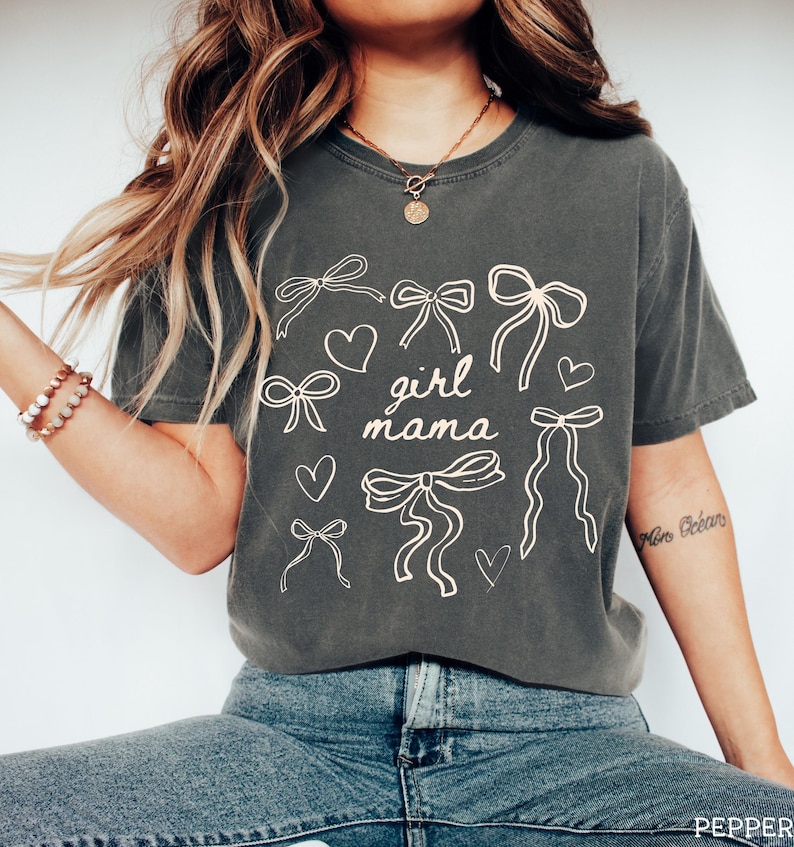 May include: A dark gray t-shirt with a graphic design of bows, hearts, and the text "girl mama".
