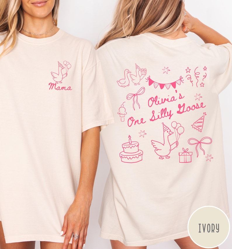 Op de afbeelding: Ivoor kleurig T-shirt met een roze gans afbeelding met ballonnen en het woord "Mama" op de voorkant. De achterkant heeft een verjaardagsthema met de tekst "Olivia's One Silly Goose" en andere illustraties.