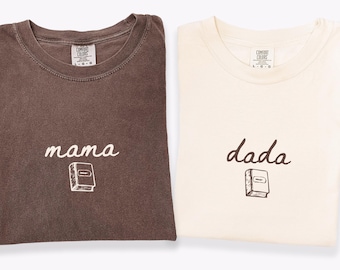 May include: Two t-shirts, one espresso and one ivory, with crew necks. The espresso shirt has the word "mama" and a book graphic. The ivory shirt has the word "dada" and a book graphic. Both shirts are Comfort Colors brand.