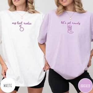 May include: A white t-shirt with the purple text my last rodeo and a diamond ring icon, and an orchid t-shirt with the purple text let's get rowdy and a cowboy boot icon. Both shirts feature short sleeves and a crew neckline.