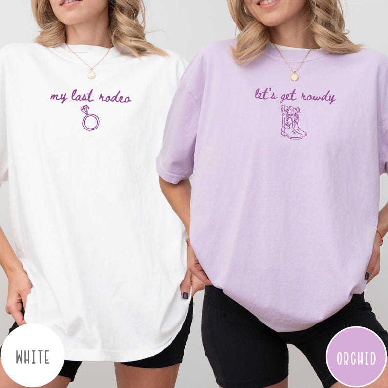 May include: A white t-shirt with the purple text my last rodeo and a diamond ring icon, and an orchid t-shirt with the purple text let's get rowdy and a cowboy boot icon. Both shirts feature short sleeves and a crew neckline.