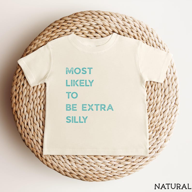 Puede incluir: Una camiseta de manga corta de color crema con el texto "MOST LIKELY TO BE EXTRA SILLY" impreso en una fuente azul claro desgastada. La prenda cuenta con un cuello redondo y un corte est&aacute;ndar, mostrando un dise&ntilde;o sencillo y limpio.