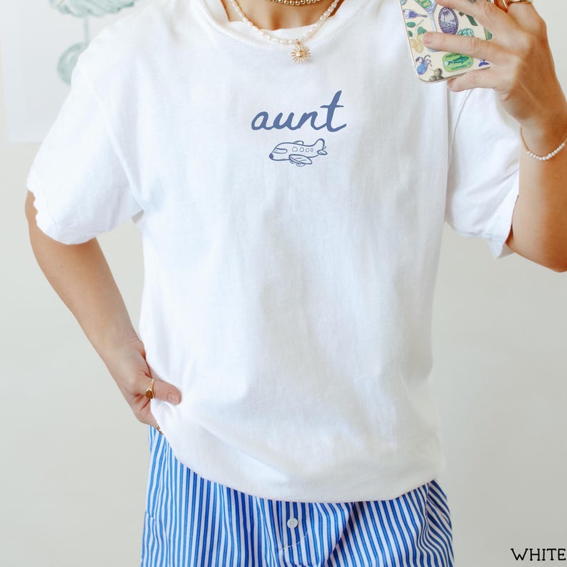 以下が含まれることがあります： 青い筆記体でauntという文字と、その下に小さな青い飛行機の線画が描かれた白い半袖Tシャツ。青と白の縦縞模様のボトムスと組み合わされています。