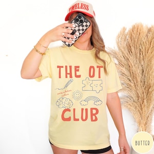 Peut inclure: Un t-shirt jaune p&acirc;le avec le texte rouge THE OT CLUB et des graphismes en ligne bleue incluant un crayon, des pi&egrave;ces de puzzle, un cerveau, un soleil et un arc-en-ciel. Le texte every milestone matters est imprim&eacute; en petit script bleu.