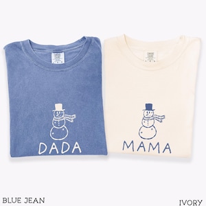 May include: Two short-sleeved t-shirts, one blue jean and one ivory, each featuring a line-art snowman graphic wearing a top hat and scarf. The blue shirt has the word DADA printed in white, while the ivory shirt has the word MAMA printed in blue.