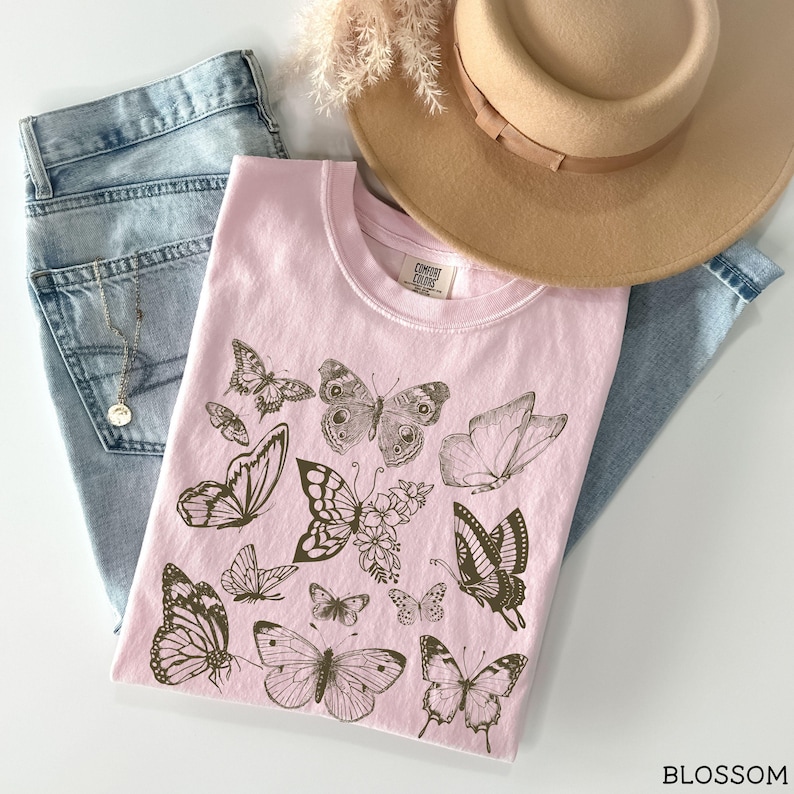 May include: A pink t-shirt with a brown butterfly design. The shirt has the text "Comfy Cozy Club" printed on the front.