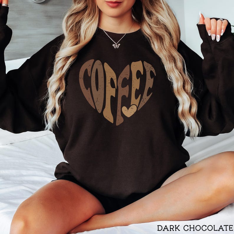 May include: Dark chocolate-colored sweatshirt with a heart-shaped design that spells out "COFFEE" in shades of brown and tan. The sweatshirt is a cozy, casual style, perfect for coffee lovers.