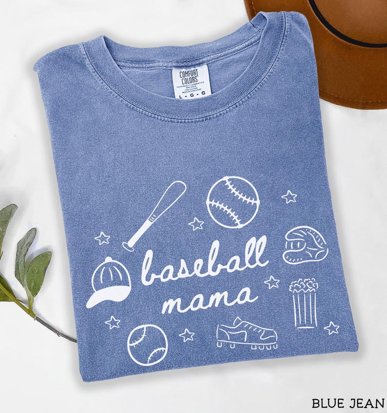 Puede incluir: Una camiseta azul claro con un dise&ntilde;o blanco de tem&aacute;tica de b&eacute;isbol. El dise&ntilde;o incluye un bate de b&eacute;isbol, una pelota de b&eacute;isbol, un guante de b&eacute;isbol, una gorra de b&eacute;isbol y el texto "baseball mama".