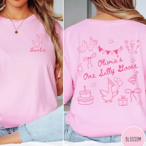 Op de afbeelding: Roze t-shirt met een afbeelding van een gans met ballonnen en het woord "Auntie" op de voorkant. De achterkant heeft een verjaardagsontwerp met de tekst "Olivia's One Silly Goose" en versieringen.