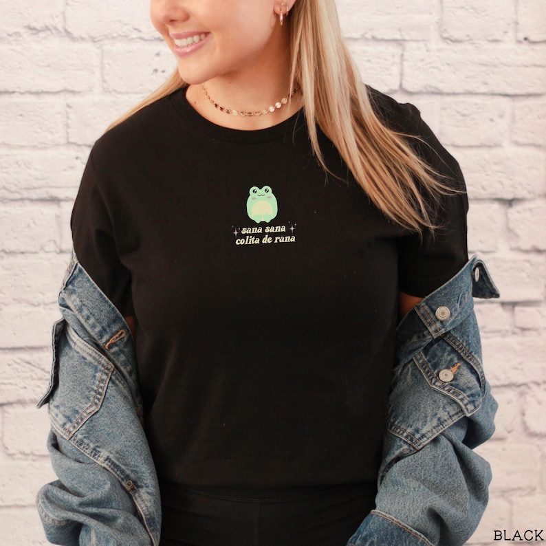 May include: Black t-shirt with a green frog graphic and the text "sana sana colita de rana" in white.