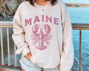 May include: A cream coloured sweatshirt with a pink lobster and the word "MAINE" printed on the front.