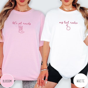 May include: A light pink t-shirt with the text let's get rowdy and a cowboy boot graphic in dark pink, and a white t-shirt with the text my last rodeo and a diamond ring graphic in dark pink, both featuring short sleeves and crew necklines.