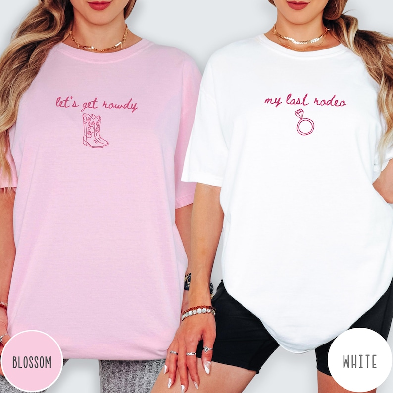 May include: A light pink t-shirt with the text let's get rowdy and a cowboy boot graphic in dark pink, and a white t-shirt with the text my last rodeo and a diamond ring graphic in dark pink, both featuring short sleeves and crew necklines.