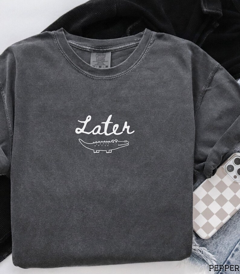 Pu&ograve; includere: Felpa girocollo grigio scuro con la scritta "Later" in corsivo bianco e una grafica di un alligatore bianco. La felpa ha un aspetto vintage e lavato. &Egrave; un capo casual per tutti i giorni. Realizzata in materiale morbido.