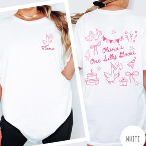 Op de afbeelding: Wit T-shirt met roze afbeeldingen. De voorkant heeft een gans met ballonnen en het woord "Mama". De achterkant toont "Olivia's One Silly Goose" met gans, taart en feestversieringen. "WHITE" staat onderaan.