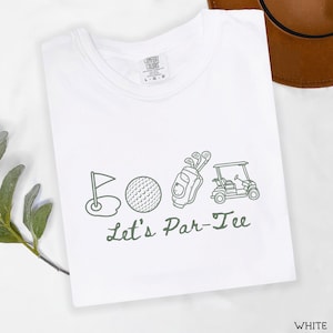 May include: White t-shirt with a green golf-themed graphic. The design includes a golf flag, golf ball, golf bag, and golf cart, with the text "Let's Par-Tee" below the images. The shirt is labeled "Comfort Colors".