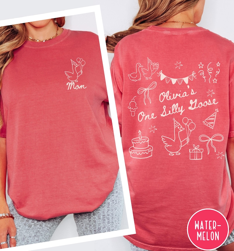 Op de afbeelding: Een koraalkleurig T-shirt met witte grafische ontwerpen. De voorkant heeft een gans met ballonnen en het woord "Mom". De achterkant toont "Olivia's One Silly Goose" met illustraties met een feestthema. Het shirt heeft een ronde halslijn.