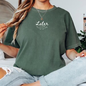 Pu&ograve; includere: T-shirt verde muschio con la scritta "Later" sopra un'illustrazione di un alligatore bianco. La maglietta ha maniche corte e una vestibilit&agrave; rilassata. Il testo e la grafica sono bianchi.
