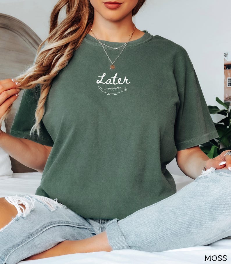Pu&ograve; includere: T-shirt verde muschio con la scritta "Later" sopra un'illustrazione di un alligatore bianco. La maglietta ha maniche corte e una vestibilit&agrave; rilassata. Il testo e la grafica sono bianchi.