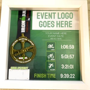 May include: Framed display featuring an Ironman Portugal Cascais 2023 medal. The gold-colored medal is displayed with race details and a green background. The frame includes text: "EVENT LOGO GOES HERE" and race times.