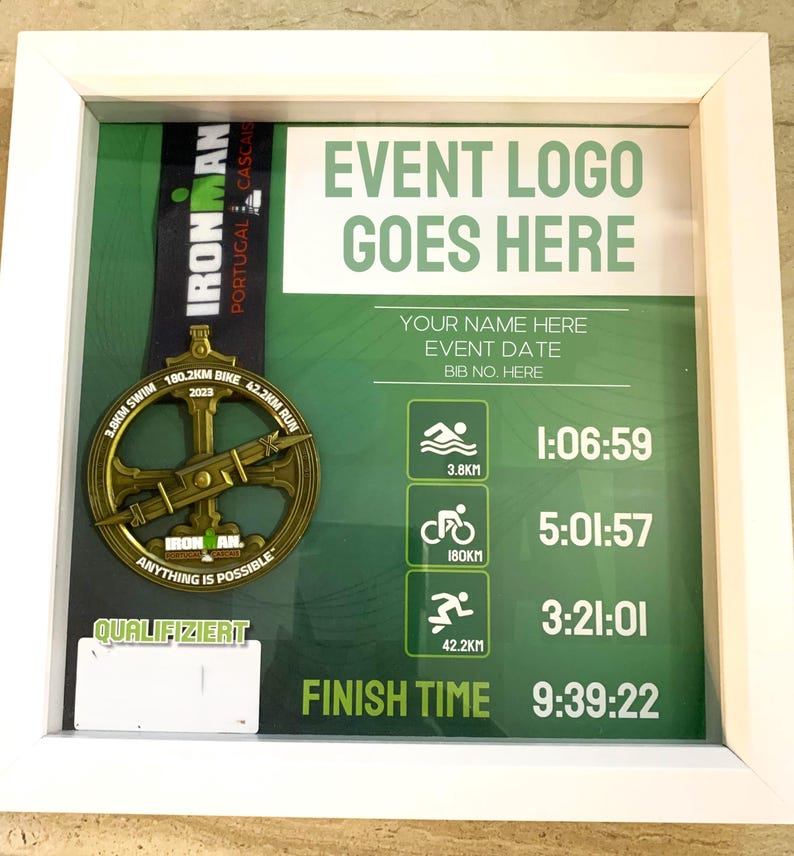 May include: Framed display featuring an Ironman Portugal Cascais 2023 medal. The gold-colored medal is displayed with race details and a green background. The frame includes text: "EVENT LOGO GOES HERE" and race times.