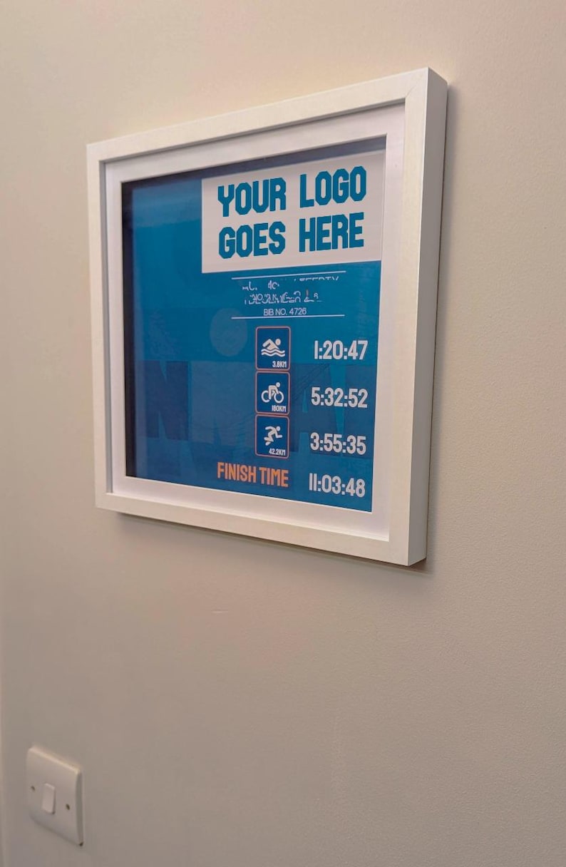 May include: A framed print with a white border displays a blue background with white text that reads "YOUR LOGO GOES HERE". Below are icons and times for swimming, biking, and running. The finish time is 11:03:48.