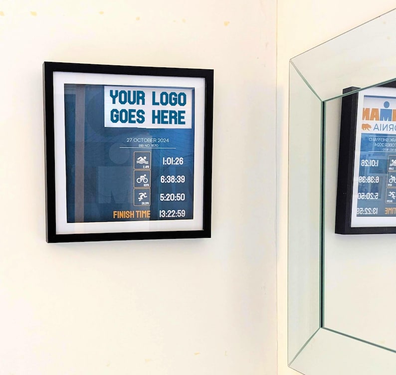 May include: A framed print with a black border, featuring the text "YOUR LOGO GOES HERE" and race data. The print includes times for swimming, cycling, and running, with a total finish time of 13:22:59. The date is October 27, 2024.