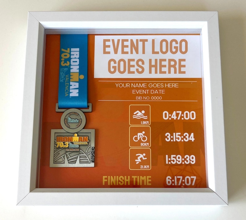 May include: A white framed display featuring an Ironman 70.3 Valencia finisher medal. The medal hangs from a blue ribbon. The display includes event details, a place for the event logo, and race times. The finish time is 6:17:07.