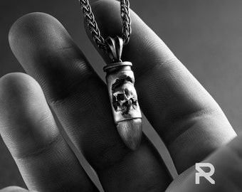 May include: A silver chain necklace with a bullet-shaped pendant featuring a detailed skull design.