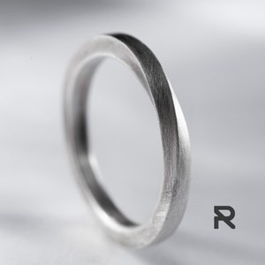 May include: A silver ring with a unique, twisted design. The ring has a brushed finish and a smooth, rounded edge.