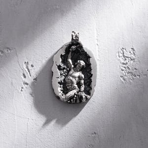 May include: Silver pendant featuring a detailed sculpture of a man breaking free from a cracked stone surface.