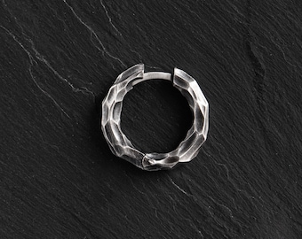 May include: A silver hoop earring with a textured, hammered finish. The earring is on a black background.