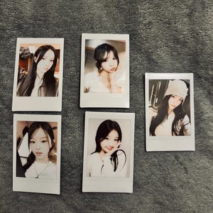 May include: Five white-framed instant photos featuring portraits of young women. The photos are arranged on a gray, textured surface. Each photo captures a different pose and expression, with varying hairstyles and outfits.