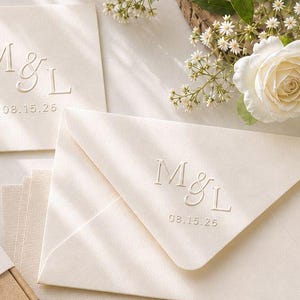 May include: An assortment of wedding stationery, including envelopes and a box, with embossed initials and dates. A light green stapler is also present. The stationery features the names "Matt & Luisa" and the date "08.30.2026".