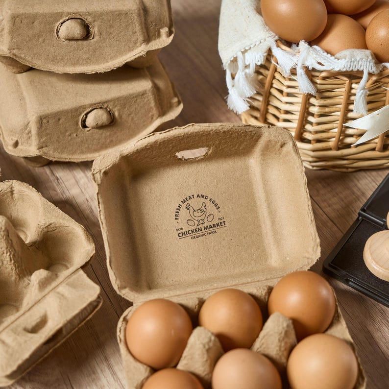 K&ouml;nnte beinhalten: Ein brauner Eierkarton aus Pappe mit sechs braunen Eiern darin. Der Karton tr&auml;gt ein Logo mit der Aufschrift "Fresh Meat and Eggs from Chicken Market Organic Farm".