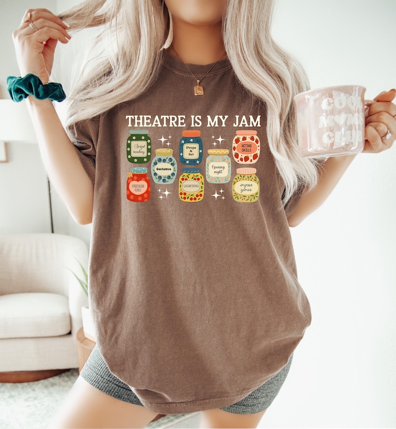 May include: Brown t-shirt with the text "THEATRE IS MY JAM" above a graphic of various jam jars. Each jar has a different label, including "Bright Reading" and "Acting Skills".