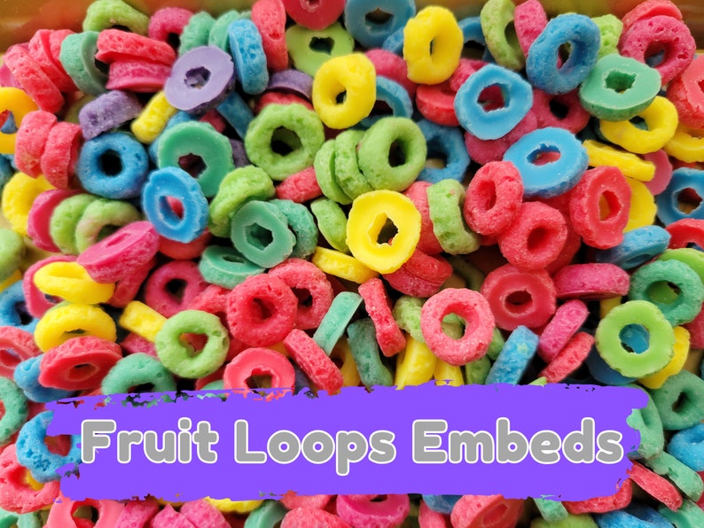 May include: A close-up of colorful, ring-shaped cereal pieces. The cereal is in various colors, including red, yellow, green, blue, and purple. The text "Fruit Loops Embeds" is displayed on a purple banner.