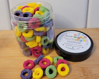 May include: A glass jar filled with colorful wax melts shaped like cereal rings. The jar has a black lid with the text "Fruit Loops" and "FOR USE IN WAX MELTERS" printed on it. The wax melts are in the colors red, yellow, green, and purple.