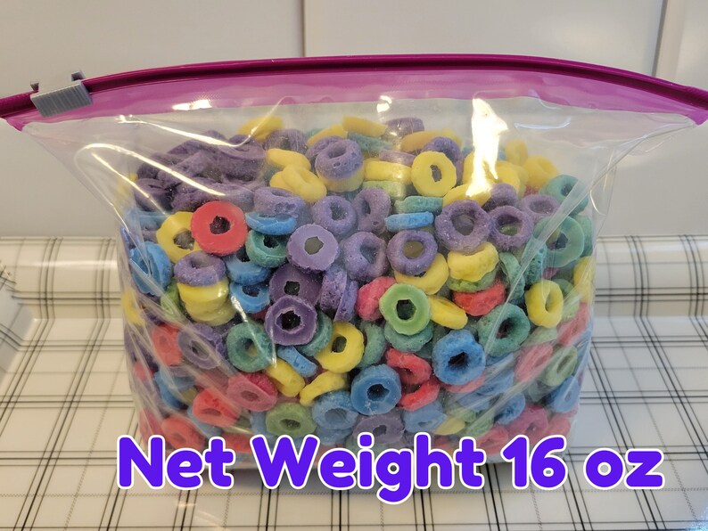 May include: A clear plastic bag filled with colorful, ring-shaped cereal. The cereal pieces are in various colors, including red, purple, yellow, and blue. The bag is sealed with a purple closure and has the text "Net Weight 16 oz".