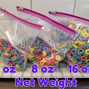 May include: Three clear plastic bags filled with colorful, ring-shaped cereal. The bags are labeled with net weights of 4 oz, 8 oz, and 16 oz. Each bag is sealed with a pink zipper and a gray clip.