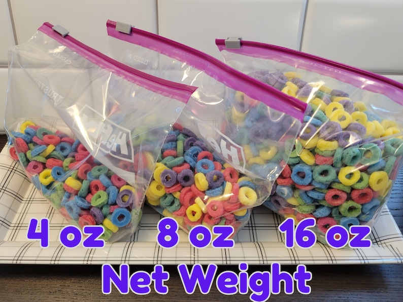 May include: Three clear plastic bags filled with colorful, ring-shaped cereal. The bags are labeled with net weights of 4 oz, 8 oz, and 16 oz. Each bag is sealed with a pink zipper and a gray clip.