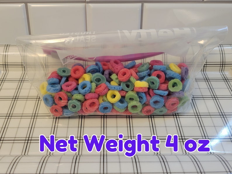 May include: A clear plastic bag filled with colorful, ring-shaped cereal. The cereal pieces are in various colors, including red, blue, yellow, and green. The text "Net Weight 4 oz" is displayed in a purple font.